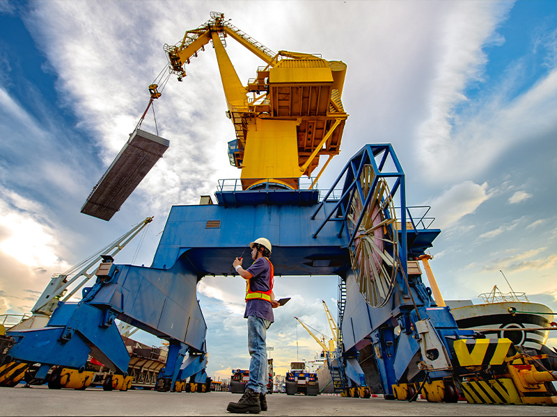 Dock worker holding container under crane in port background in an industrial warehouse