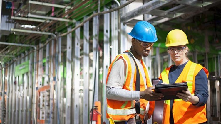 Two people in safety gear review data on multiple screens