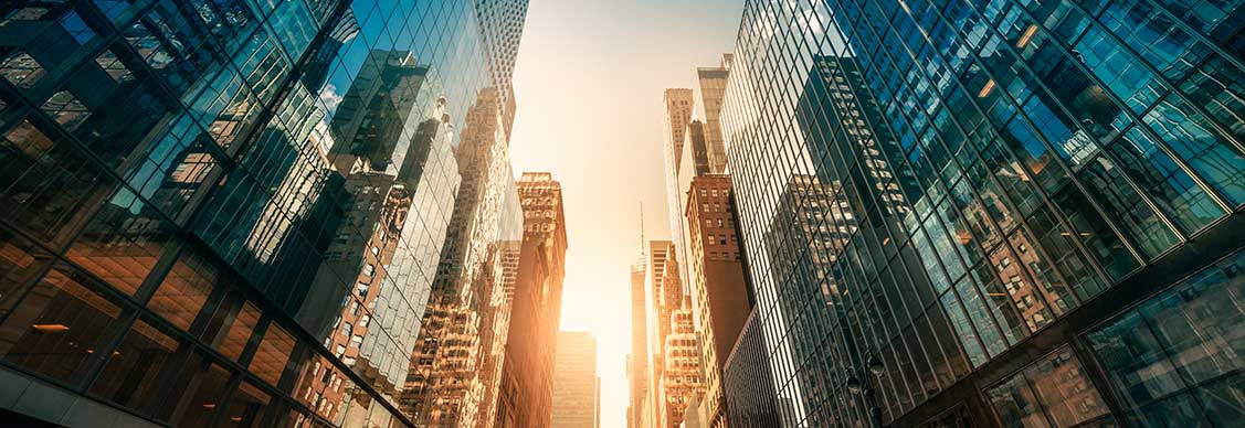 City skyline reflected on buildings lining a street with a setting sun