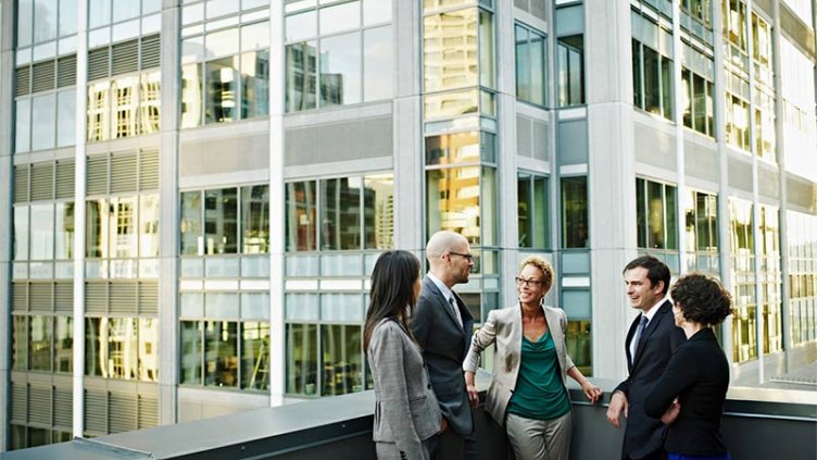 Group of coworkers standing in discussion on deck of office buildings in background