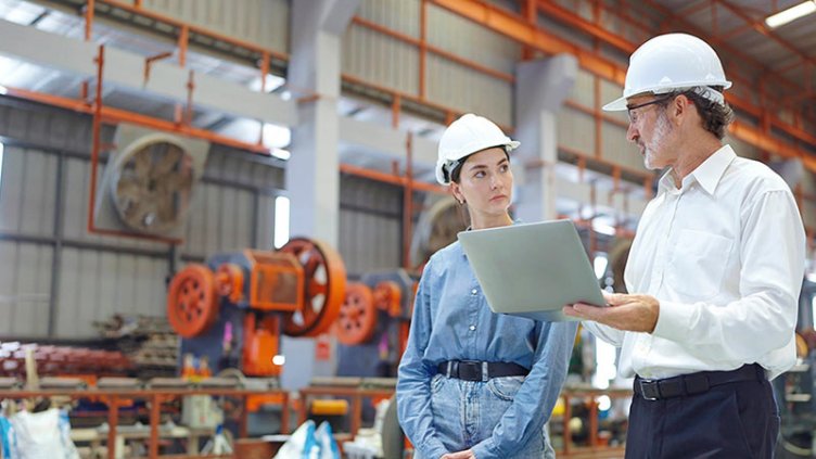 engineer man and woman manager leader wearing helmet and holding laptop walking in factory talking and discussing for work