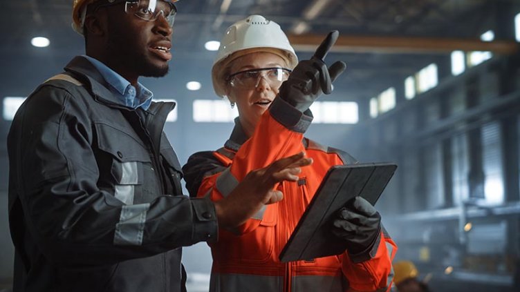 African-American worker talking with Caucasian businesswoman and looking at a tablet in a factory