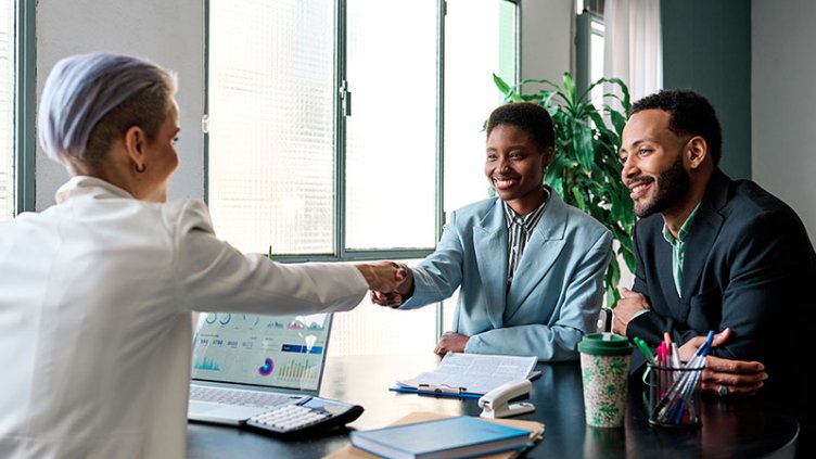 Man and woman meeting with a financial planner . The women is shaking hands with the financial planner.