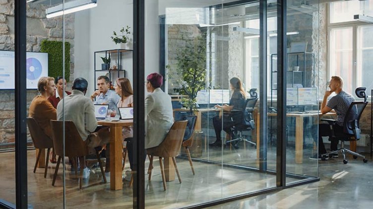 Office space with people in a glass meeting room and other employees working at their desks