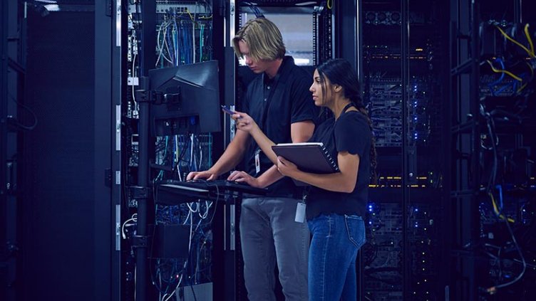 Two individuals standing in front of a server rack, engaged in discussion about technology and data management.