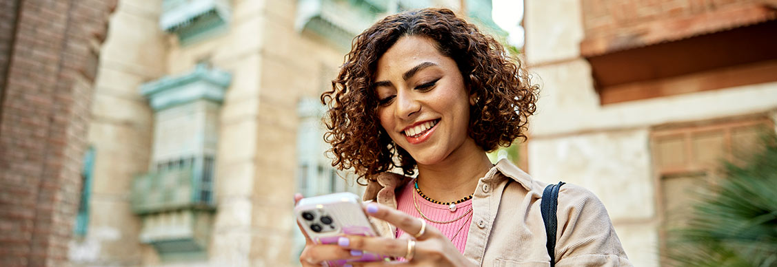 Young woman surrounded by buildings looking at smart phone to access directions and information in a historic city.