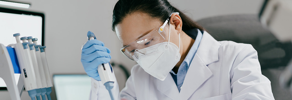 A female scientist in a lab coat and mask conducts an experiment with a test tube in a laboratory environment.