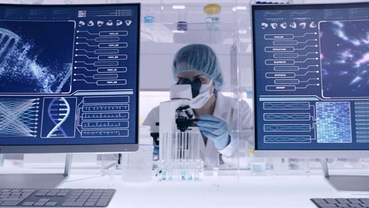 Life sciences laboratory with a scientist at work between two computer screens showing scientific data.