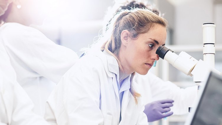 A woman focuses on a microscope