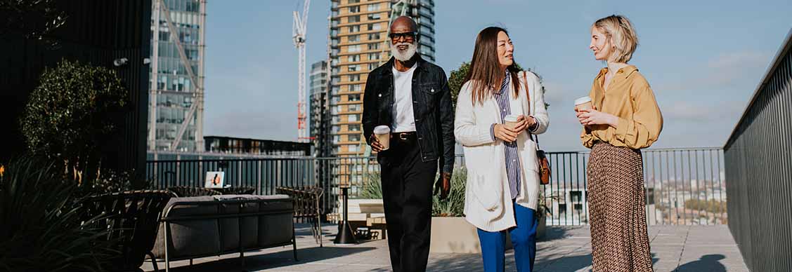 Three people in smart-casual business attire walk together on a roof top