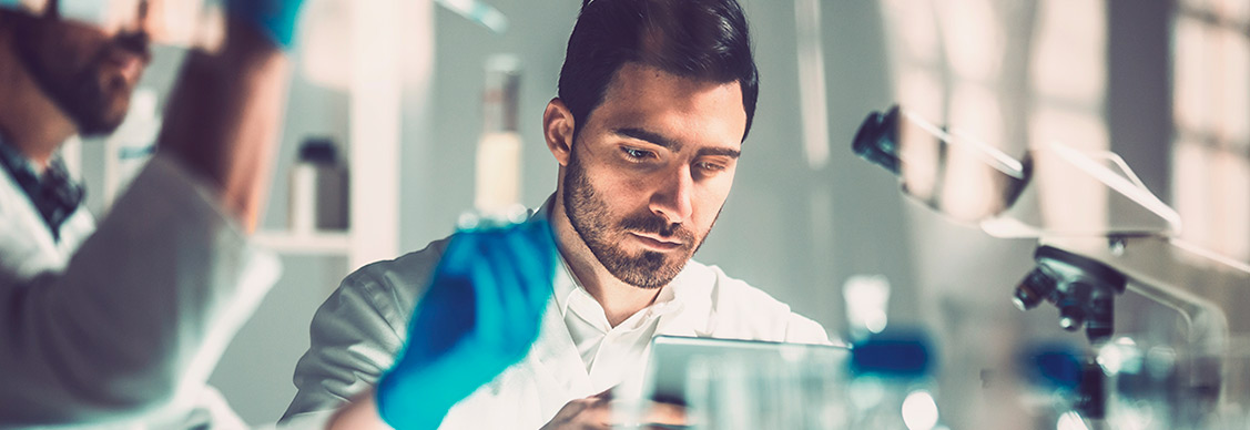 Two men wearing lab coats studying a tablet together, demonstrating collaboration in a scientific environment.